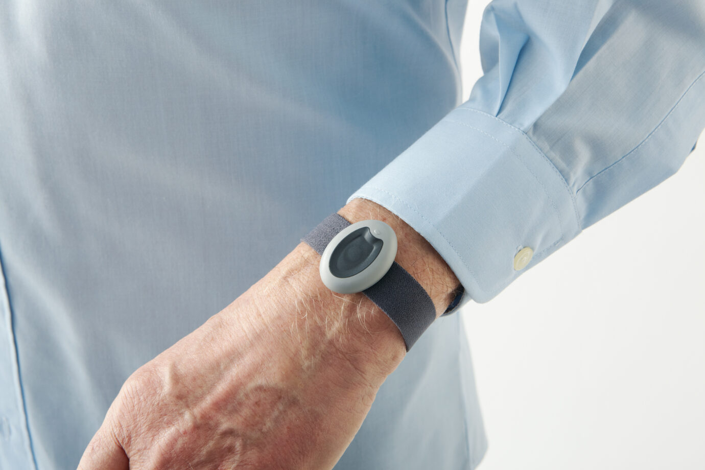 Hand mit grauem Hausnotruf-Armband mit Notfallknopf am Handgelenk, tragbarer Sturzalarm für Senioren.
