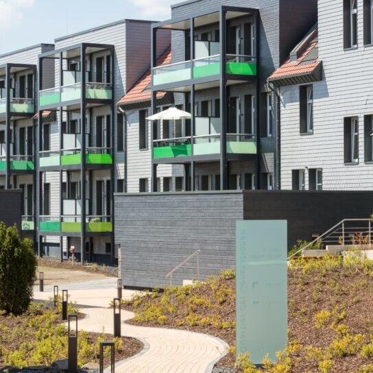 Moderne Wohnanlage mit grünen Balkonen, grauer Schieferfassade und gepflegten Wegen in der Außenanlage