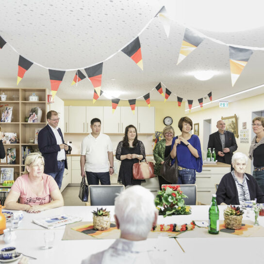 Besucher und Senioren im Gemeinschaftsraum eines Pflegeheims, Treffen bei Kaffee, dekoriert mit Deutschlandfahnen.