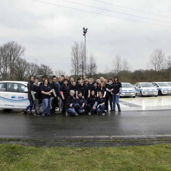 APD-Team vor Dienstwagenflotte auf Außengelände; Gruppenfoto bei bedecktem Himmel.