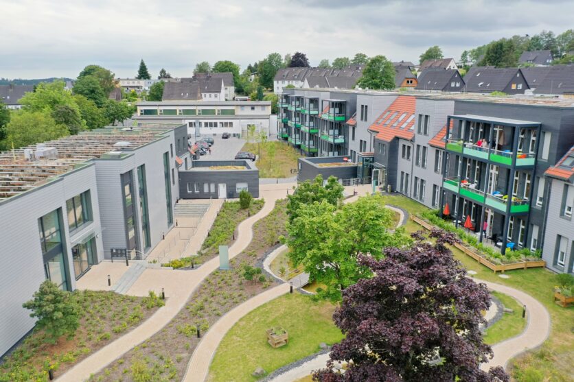 Moderne Wohnanlage mit begrün-tem Innenhof, geschwungenen Wegen und Balkonen, Luftaufnahme des Mehrfamilienquartiers